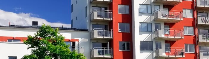 Vy över en nybyggd flerfamiljsfastighet med ett hus i olika höjder och röd och vitmålad fasad.