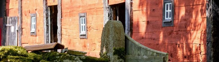 En rödmålad äldre lada med svarta knutar och portar i ett vårlandskap i Öländsk charm