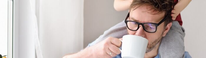 En man dricker morgonkaffe och tittar på en datorskärm samtidigt som en glad pojke sitter på hans axlar. i en grå ruta står texten välkommen till vår nya kundwebb mbabs logotyp finns i vitt i bildens nedre hörn.