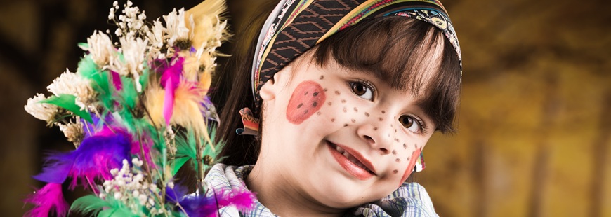 En flicka utklädd till påskakärring håller ett ris med påskfjärdrar i glada färger.