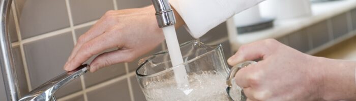 En kvinna fyller en karaff med vatten under kökskranen